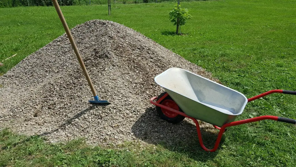 Grey wheelbarrow and shovel next to a pile of gravel